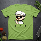 Lime Green t-shirt with a cartoon character chef and 'HEARD' text on a dark surface.