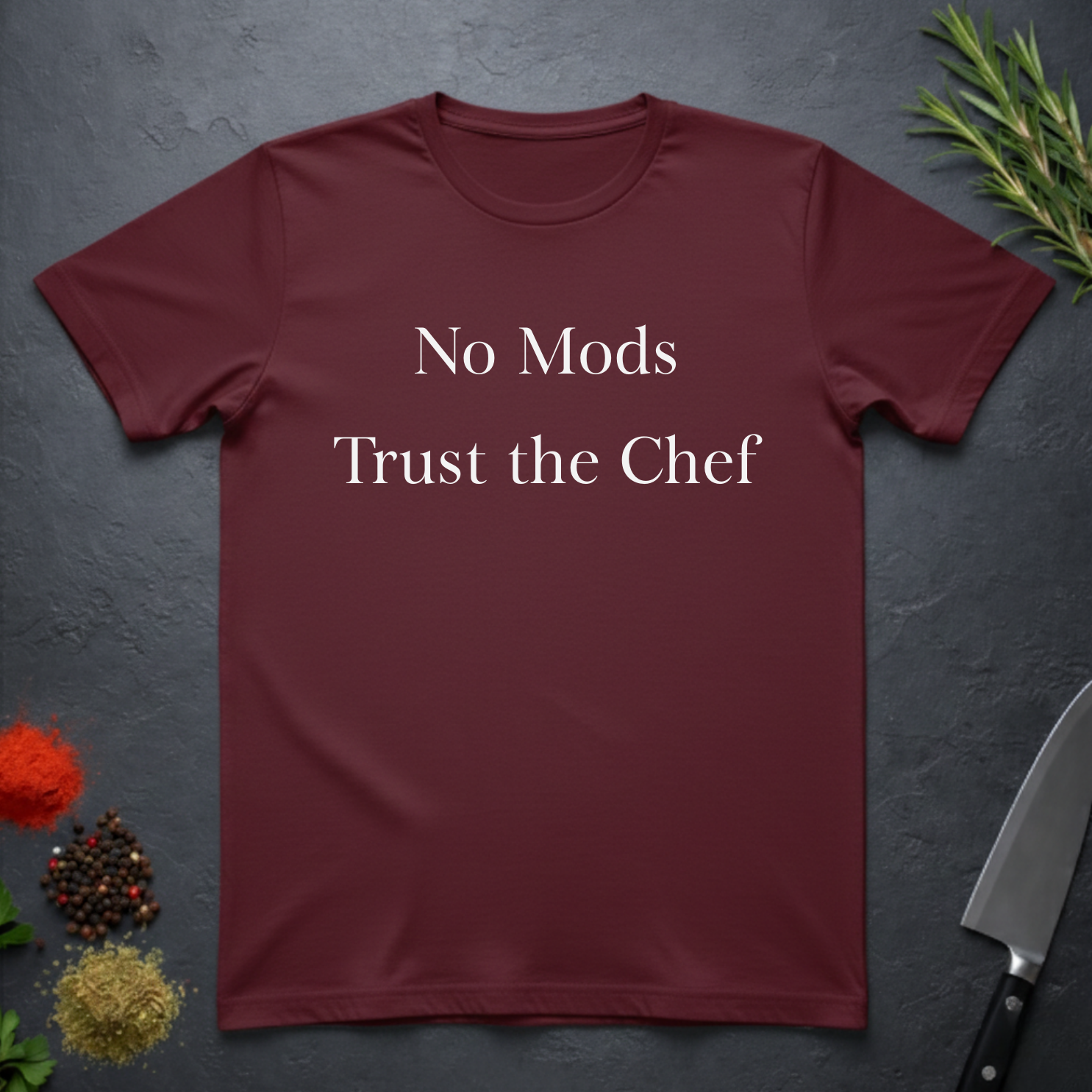 Maroon t-shirt with 'No Mods Trust the Chef' text on a dark surface with kitchen items.