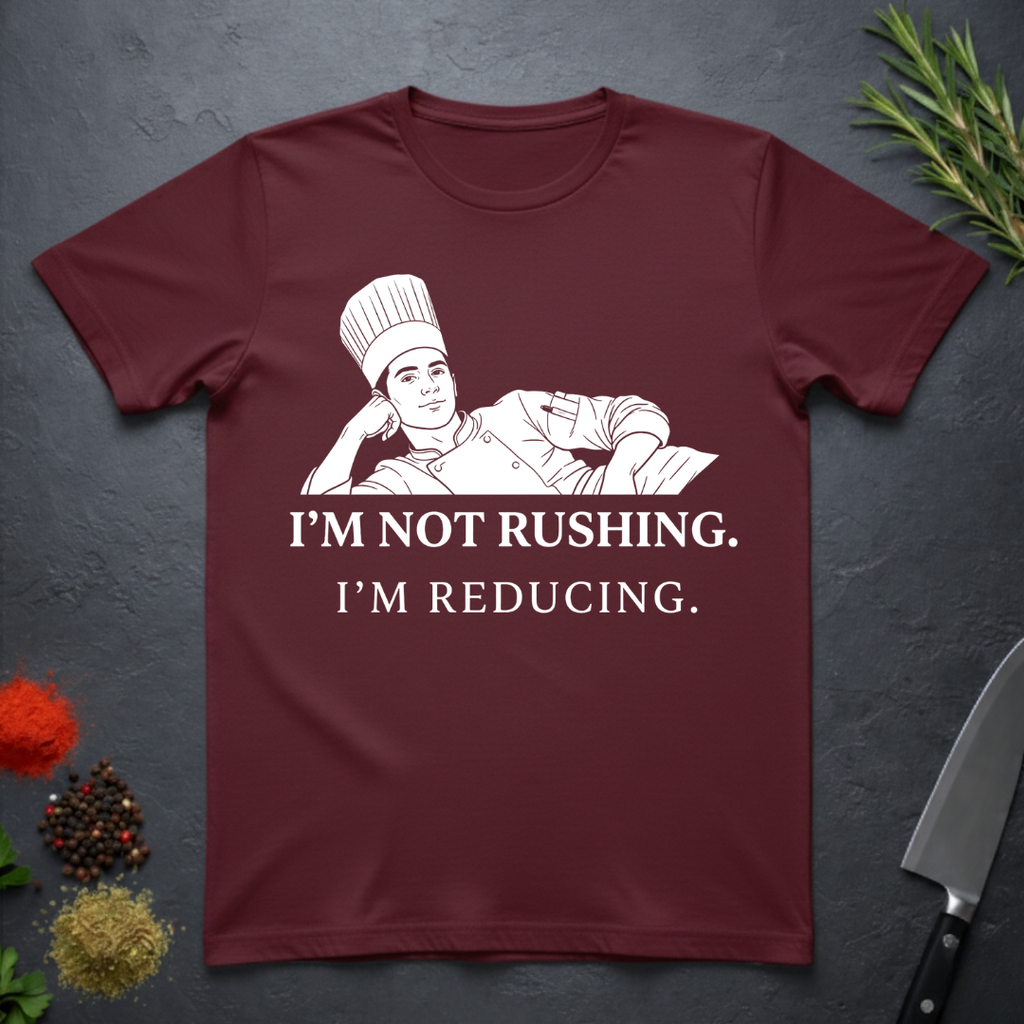 Maroon t-shirt with a chef graphic and text on a dark surface with kitchen items.