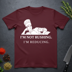 Maroon t-shirt with a chef graphic and text on a dark surface with kitchen items.