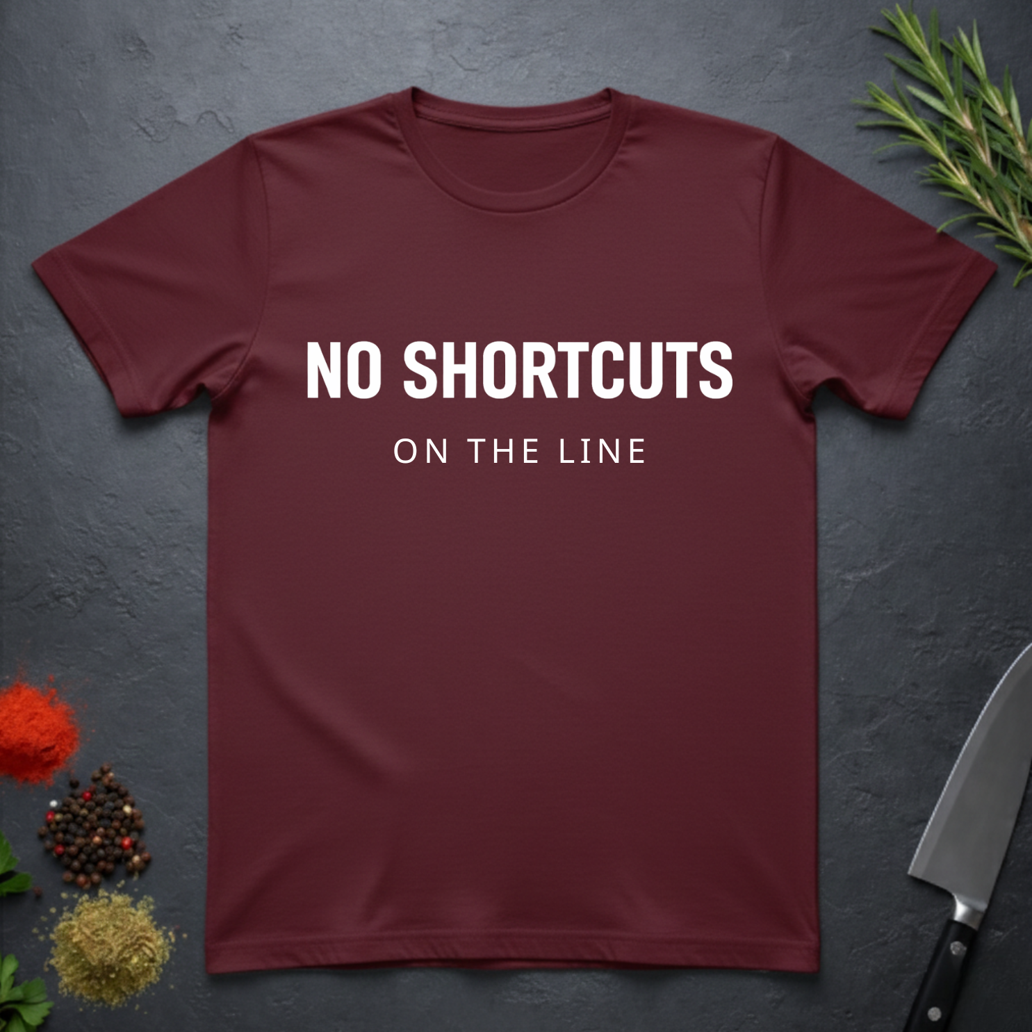 Maroon t-shirt with 'NO SHORTCUTS ON THE LINE' text on a dark surface with decorative elements.