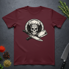 Maroon t-shirt with skull in chef hat with crossed knifes graphic on a dark surface.