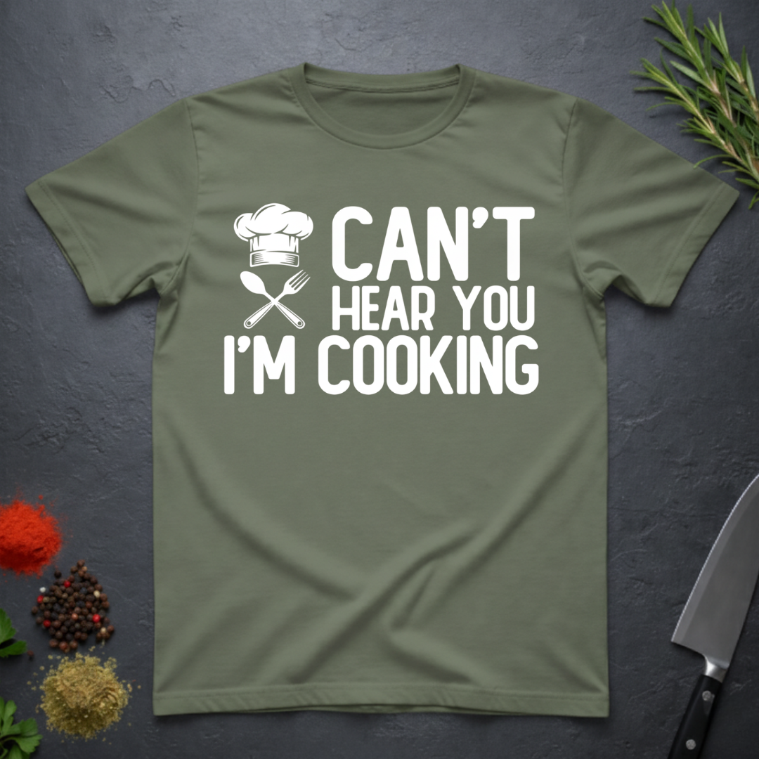 Military Green t-shirt with 'Can't Hear You I'm Cooking' text on a dark surface with kitchen items.