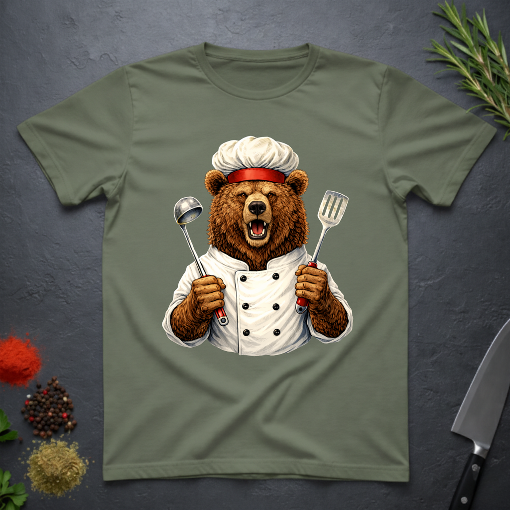 Sage green t-shirt with a grizzly bear chef holding utensils design on a dark surface.