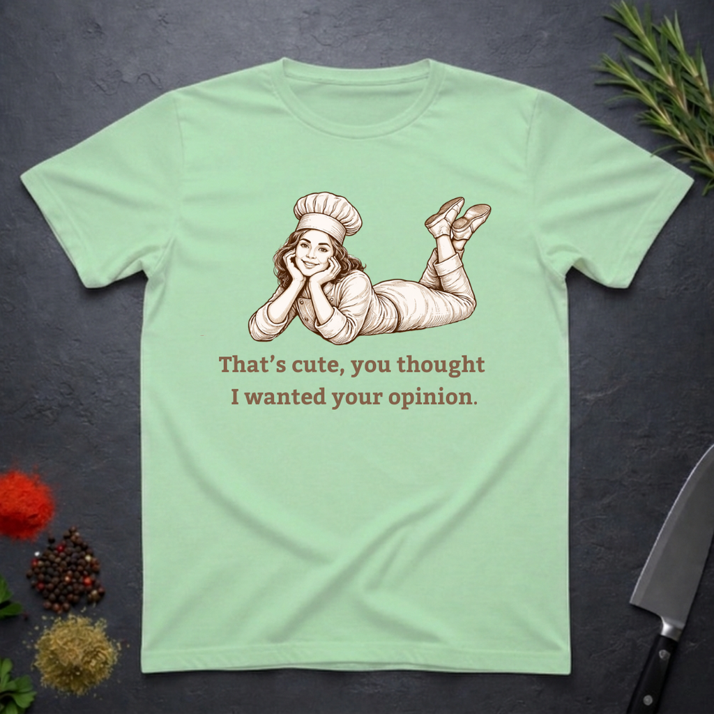 Mint green t-shirt with a graphic of a woman in a chef's outfit and text "That's cute, you thought I wanted your opinion." On a dark surface.