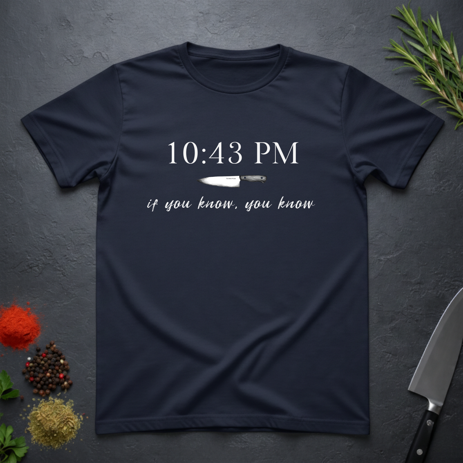 Navy blue t-shirt with knife graphic and text "10:43 PM - if you know, you know" on a dark surface.