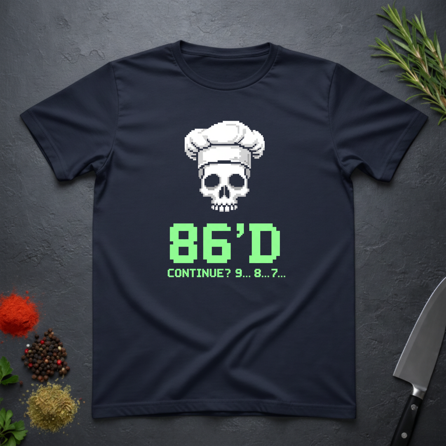 Navy blue t-shirt with a skull wearing a chef's hat and text "86'd Continue? 9...8....7..." on a dark surface.