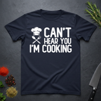 Navy blue t-shirt with 'Can't Hear You I'm Cooking' text on a dark surface with kitchen items.