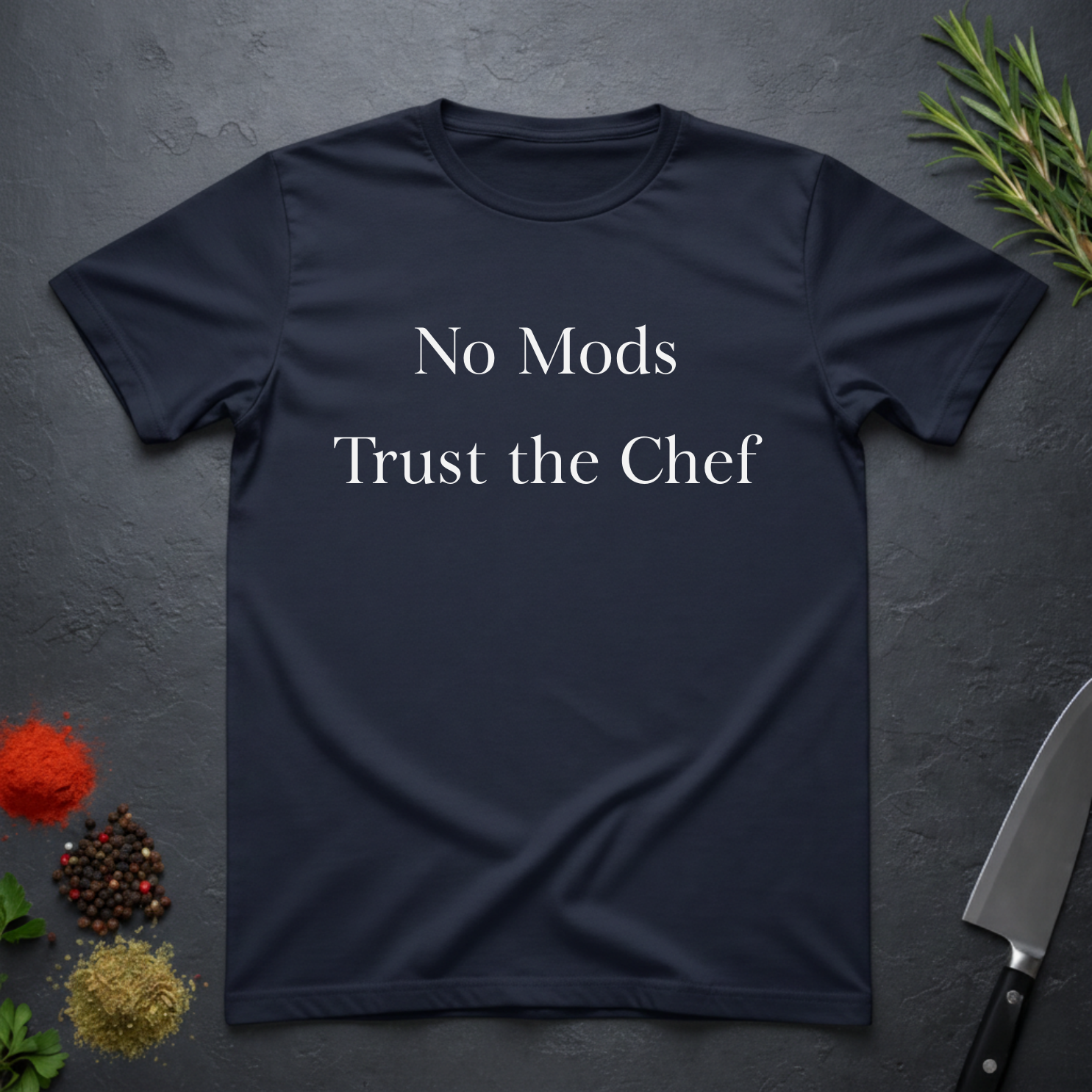 Navy blue t-shirt with 'No Mods Trust the Chef' text on a dark surface with kitchen items.