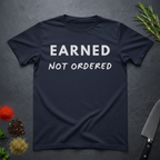 Navy blue t-shirt with 'Earned Not Ordered' text on a dark surface with decorative elements.