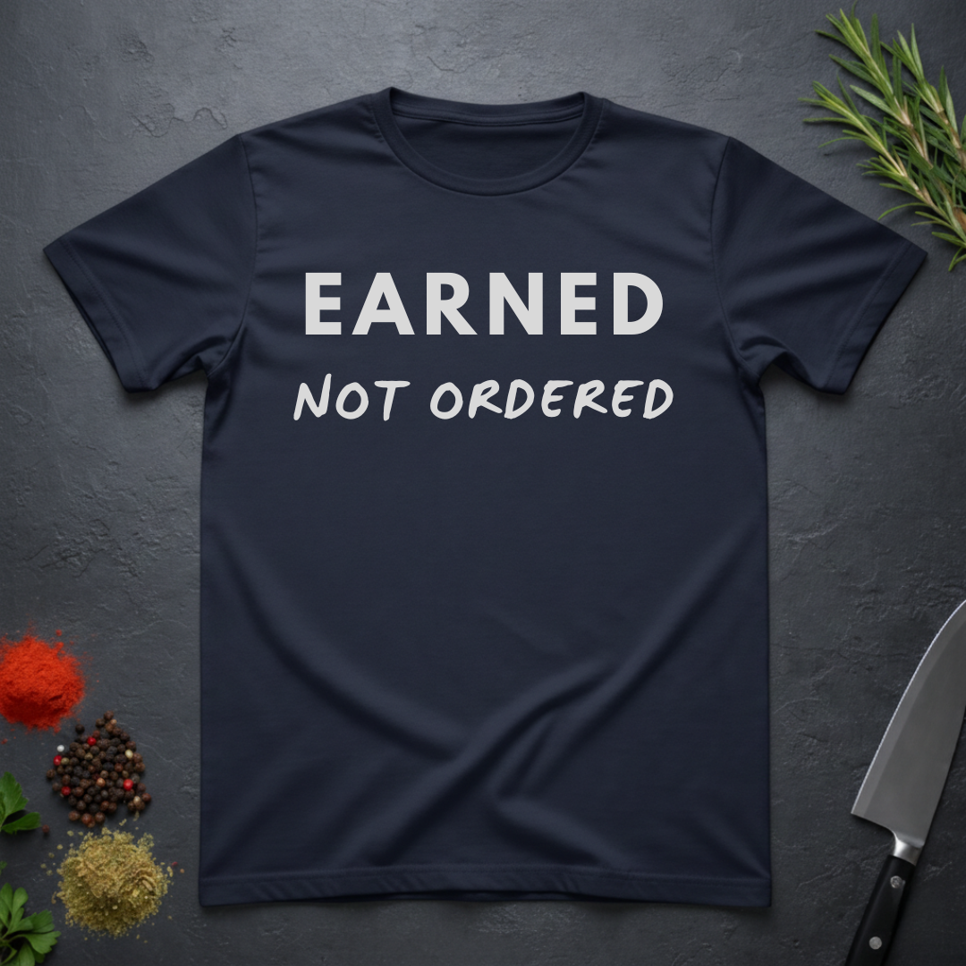 Navy blue t-shirt with 'Earned Not Ordered' text on a dark surface with decorative elements.