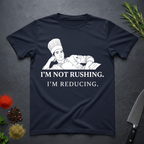 Navy blue t-shirt with a graphic of a chef and text 'I'm not rushing. I'm reducing.' on a dark surface.