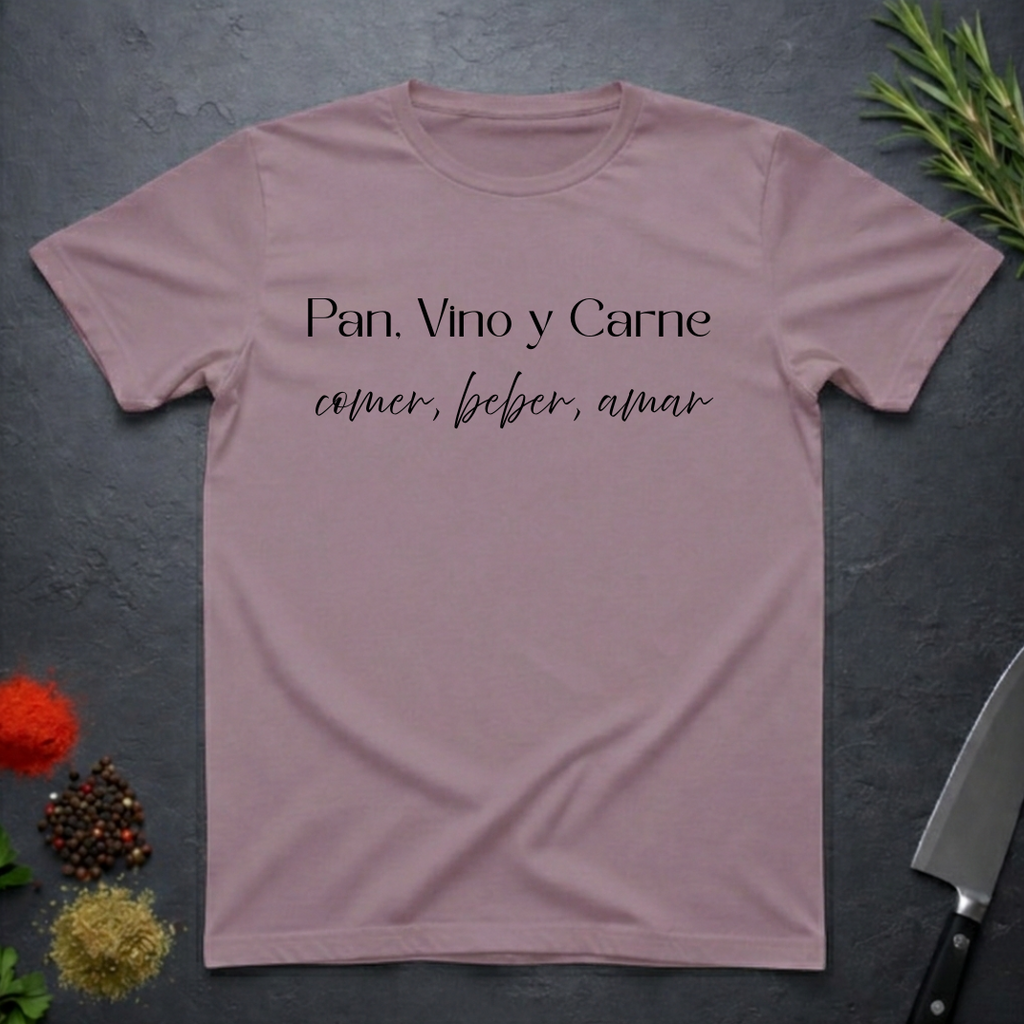 Paragon colored t-shirt with Spanish text "Pan, Vino y Carne" on a dark surface with decorative elements. 