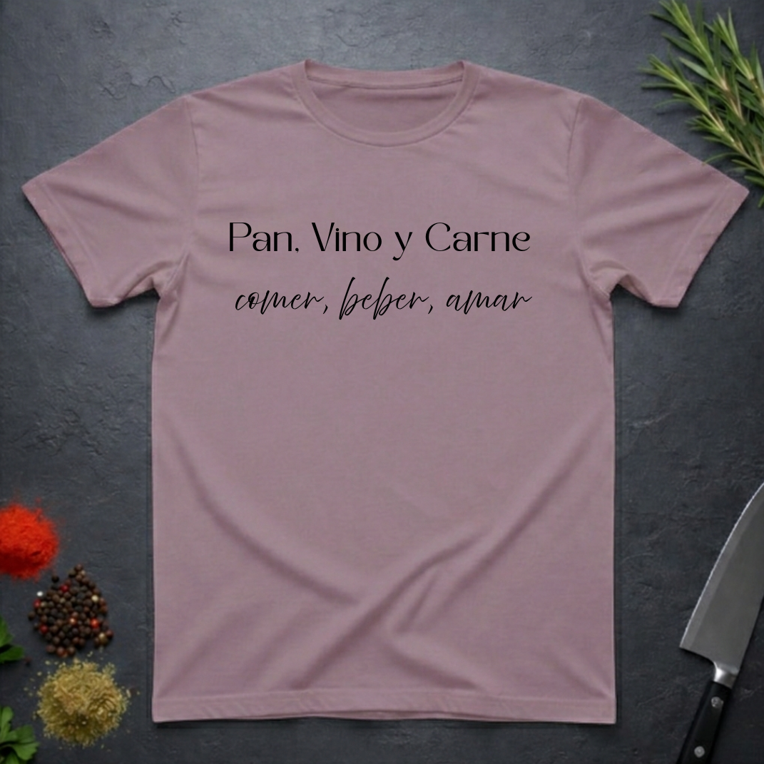 Paragon colored t-shirt with Spanish text "Pan, Vino y Carne" on a dark surface with decorative elements. 