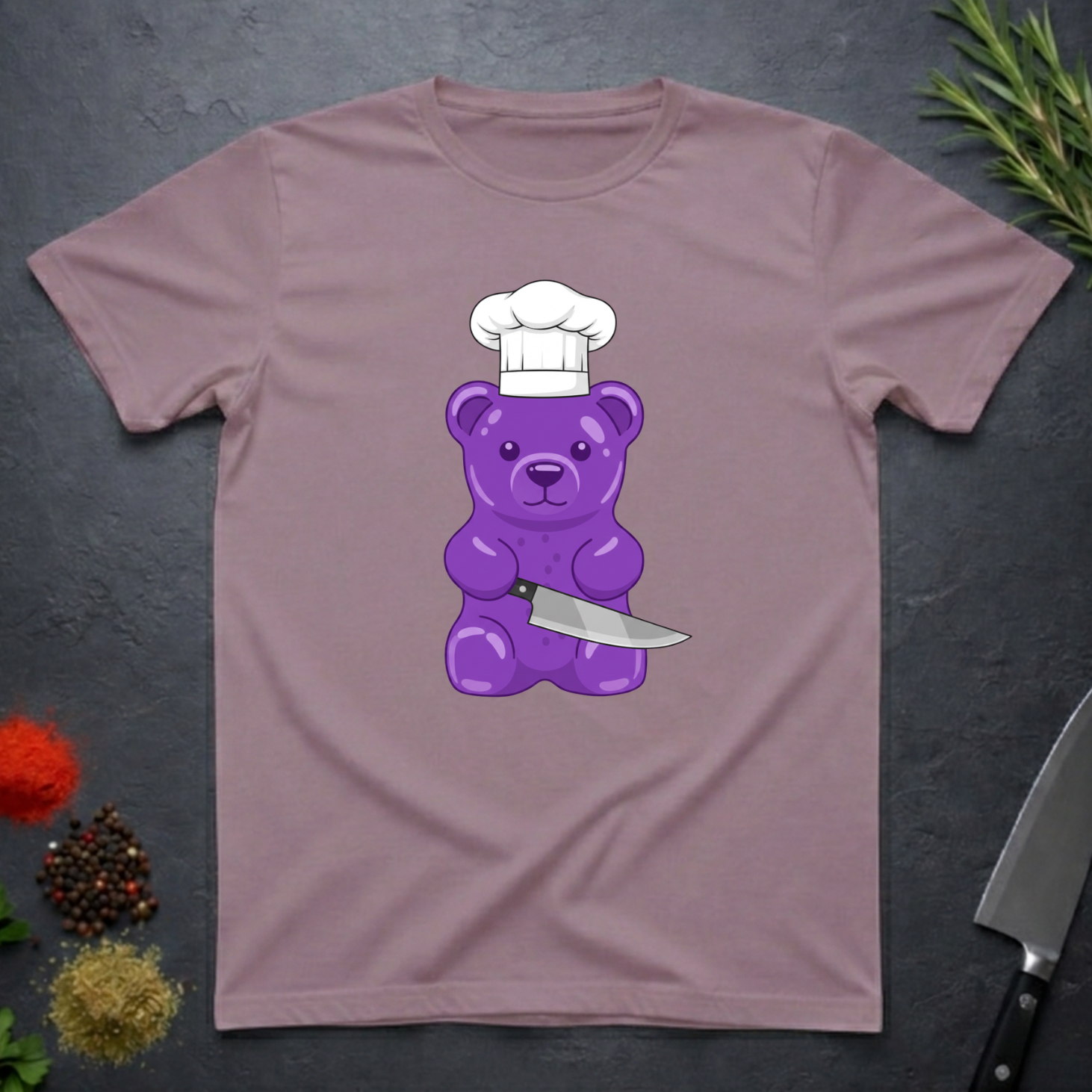 Paragon colored t-shirt with a purple bear wearing a chef's hat and holding a knife on a dark surface.