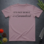 Paragon colored t-shirt with text 'IT'S NOT BURNT. IT'S Caramelized.' on a dark surface with kitchen items.
