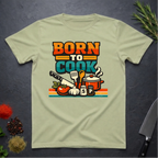 Pistachio green t-shirt with 'Born to Cook' graphic on a dark surface with kitchen items.