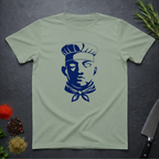 Sage Green t-shirt with dark blue graphic chef face design on a dark surface with kitchen items.