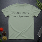 Sage Green t-shirt with Spanish text "Pan, Vino y Carne" on a dark surface with decorative elements. 