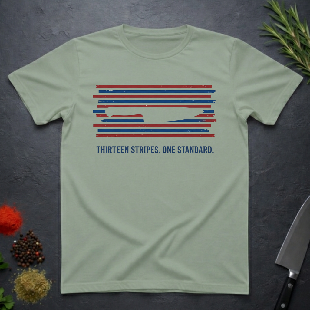 Sage green t-shirt with 13 red, white, and blue stripes with a cut out (negative space) image of a chef's knife and text "THIRTEEN STRIPES. ONE STANDARD." on a dark surface.