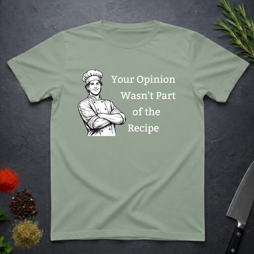 Sage green t-shirt with a male chef graphic and text "Your Opinion Wasn't Part of the Recipe" on a dark surface with kitchen items.