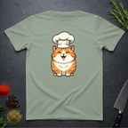 Sage green t-shirt with an orange cartoon cat wearing a chef's hat on a dark surface.