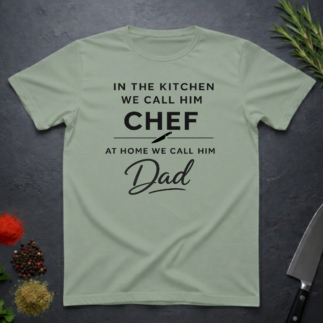 Sage Green t-shirt for Father's with text "In the kitchen we call him Chef - At home we call him Dad" on a dark surface.
