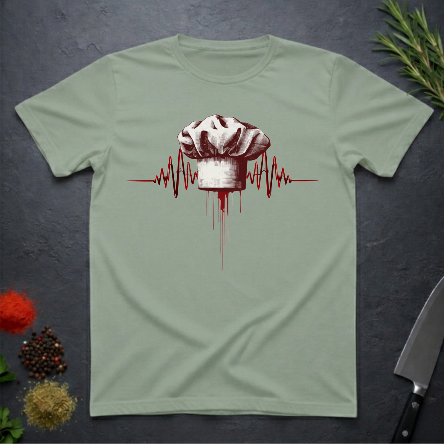 Sage Green t-shirt with a chef hat and heartbeat design on a dark surface with kitchen items.
