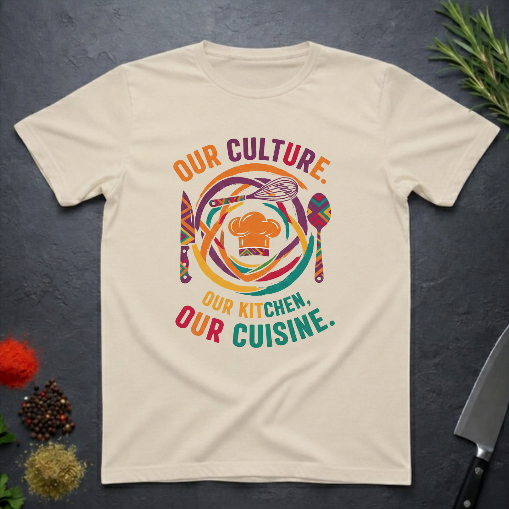 Sand colored t-shirt with colorful African graphic and text "Our Culture Our Kitchen, our Cuisine: on a dark surface.