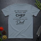 Stone blue t-shirt for Father's with text "In the kitchen we call him Chef - At home we call him Dad" on a dark surface.