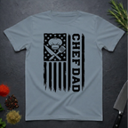 Stone blue t-shirt with American flag and text 'CHEF DAD' design on a dark surface with kitchen items.