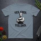 Stone blue t-shirt with a graphic of a chef and text 'YES, CHEF. YES, DAD.' on a dark surface.