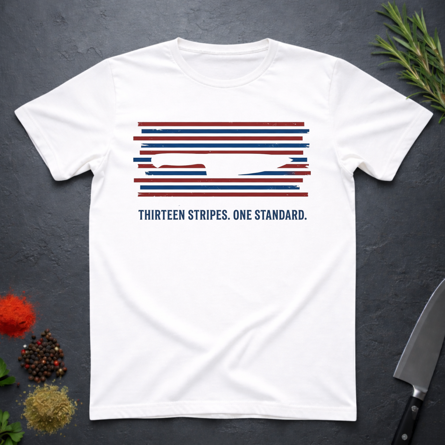 White t-shirt with 13 red, white, and blue stripes with a cut out (negative space) image of a chef's knife and text "THIRTEEN STRIPES. ONE STANDARD." on a dark surface.