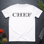White t-shirt with 'CHEF' printed in a decorative serif text on a dark surface with kitchen items.