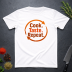 White t-shirt with bold text 'Cook. Taste. Repeat.' text inside of a large repeat symbol on a dark surface.