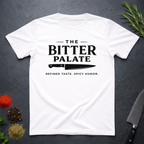 White t-shirt with 'The Bitter Palate' logo on a dark surface with kitchen items.