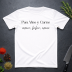 White t-shirt with Spanish text "Pan, Vino y Carne" on a dark surface with decorative elements. 