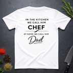 White t-shirt for Father's with text "In the kitchen we call him Chef - At home we call him Dad" on a dark surface.