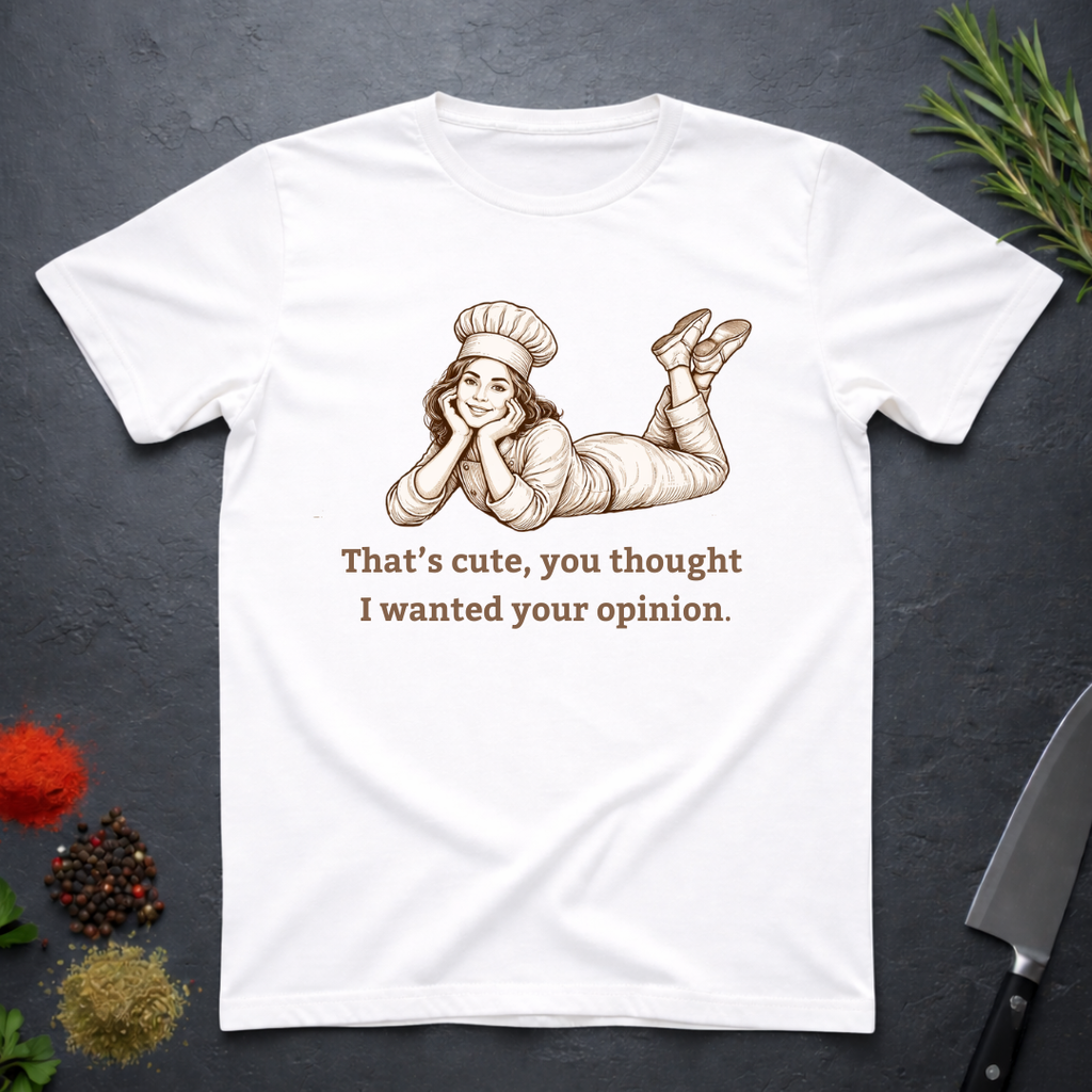 White t-shirt with a graphic of a woman in a chef's outfit and text "That's cute, you thought I wanted your opinion." On a dark surface.