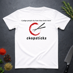 White t-shirt with Chopsticks graphic and text "I judge people by how they hold their chopsticks" on a dark surface with kitchen items.