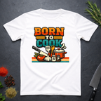 White t-shirt with 'Born to Cook' graphic design on a dark surface with kitchen items.