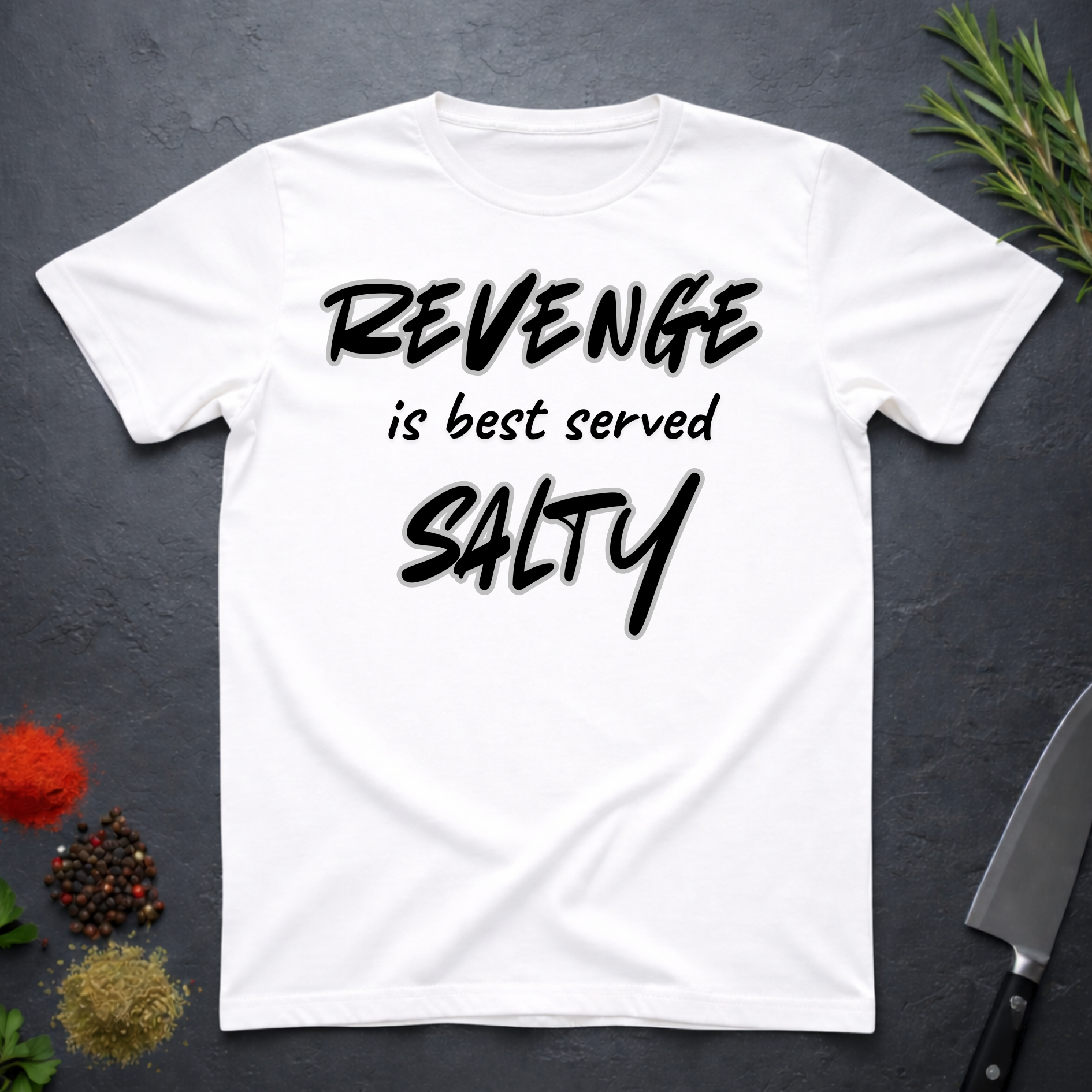 White t-shirt with 'REVENGE is best served SALTY' text on a dark surface.