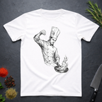 White t-shirt with a artistic graphic of a chef sprinkling salt into a pan with fire on a dark surface with kitchen items.