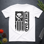 White t-shirt with American flag and text 'CHEF DAD' design on a dark surface with kitchen items.
