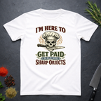 White t-shirt with skull and knife graphic and text "I'm Here to Get Paid the Play with Sharp objects" on a dark surface