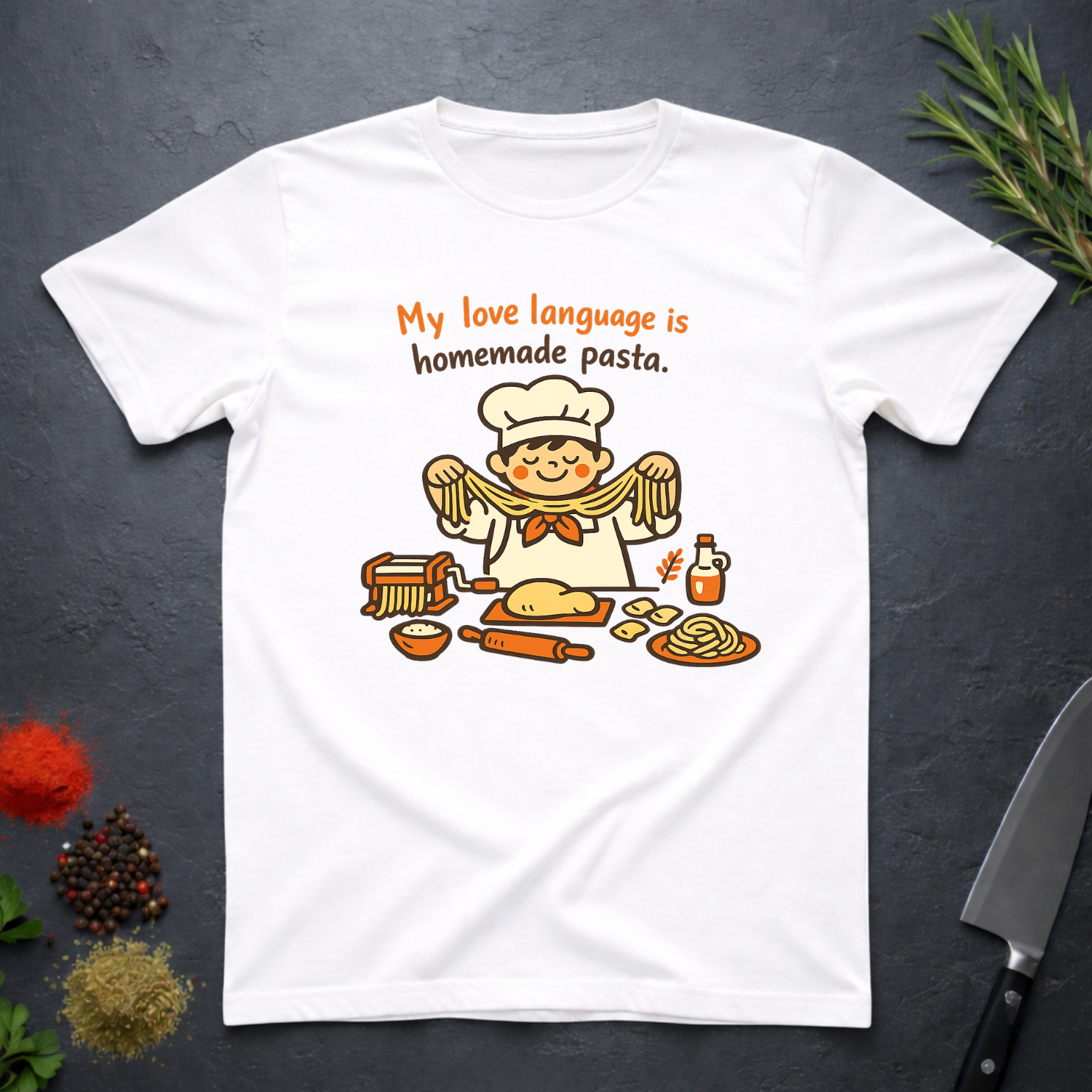 White t-shirt with a cartoon chef and pasta graphic on a dark surface with text "My love language is homemade pasts" on a dark surface.