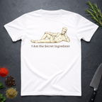 White t-shirt with a graphic of a chef lying on his side and text 'I Am the Secret Ingredient' on a dark surface with kitchen items.