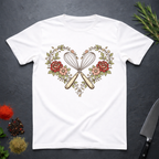 White t-shirt with a design of crossed whisk and spatula inside a heart shape surrounded by flowers and roses on a dark surface.