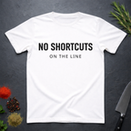 White t-shirt with 'NO SHORTCUTS ON THE LINE' text on a dark surface with decorative elements.